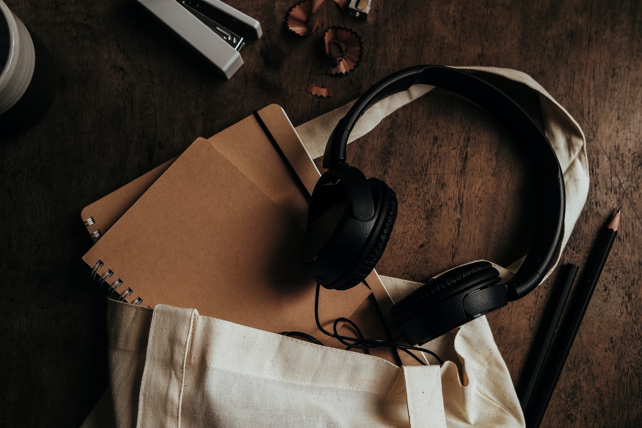 Notebooks containing blog post ideas are tucked inside a beige tote bag beneath headphones.