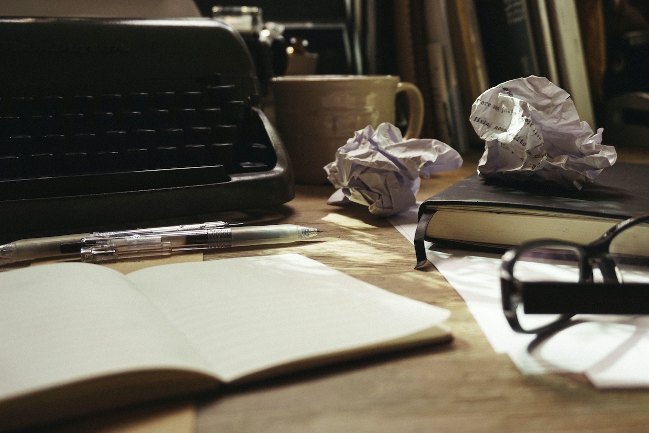 A pile of papers with brand copywriting sits beside a typewriter.