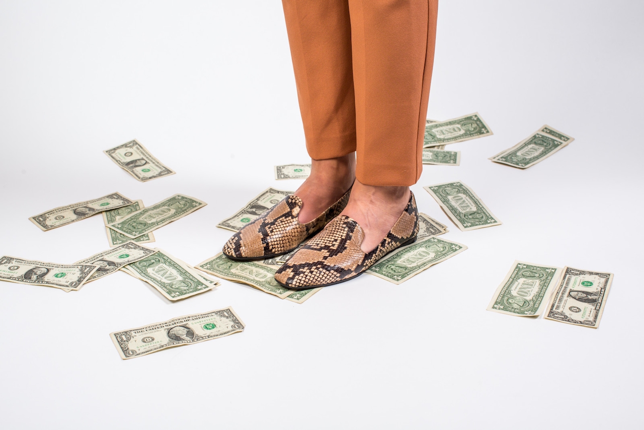 A person in aligator-print shoes stands on one dollar bills while discussing a marketing channel strategy.