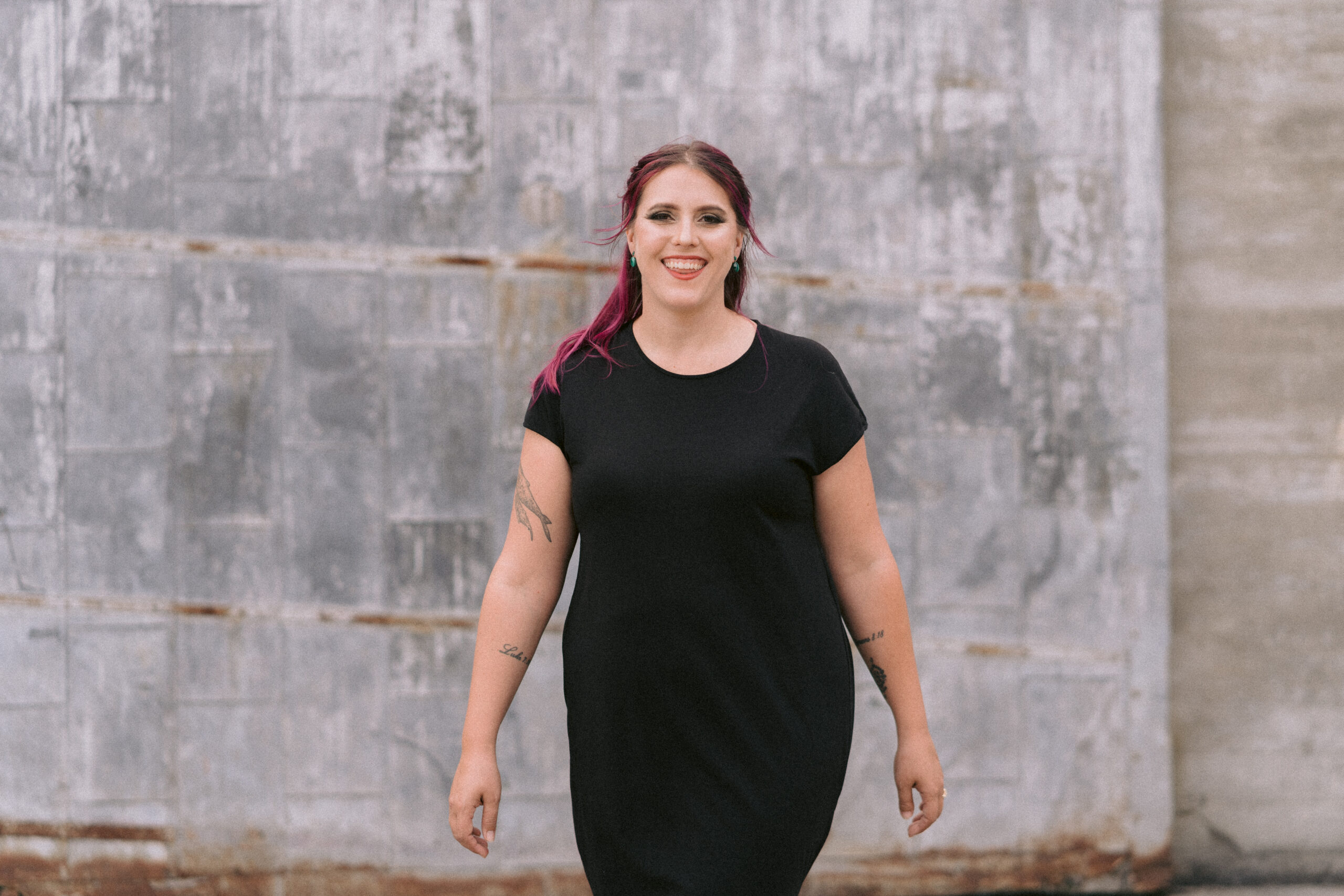 An SEO copywriter in a black dress smiles in front of a stone wall.