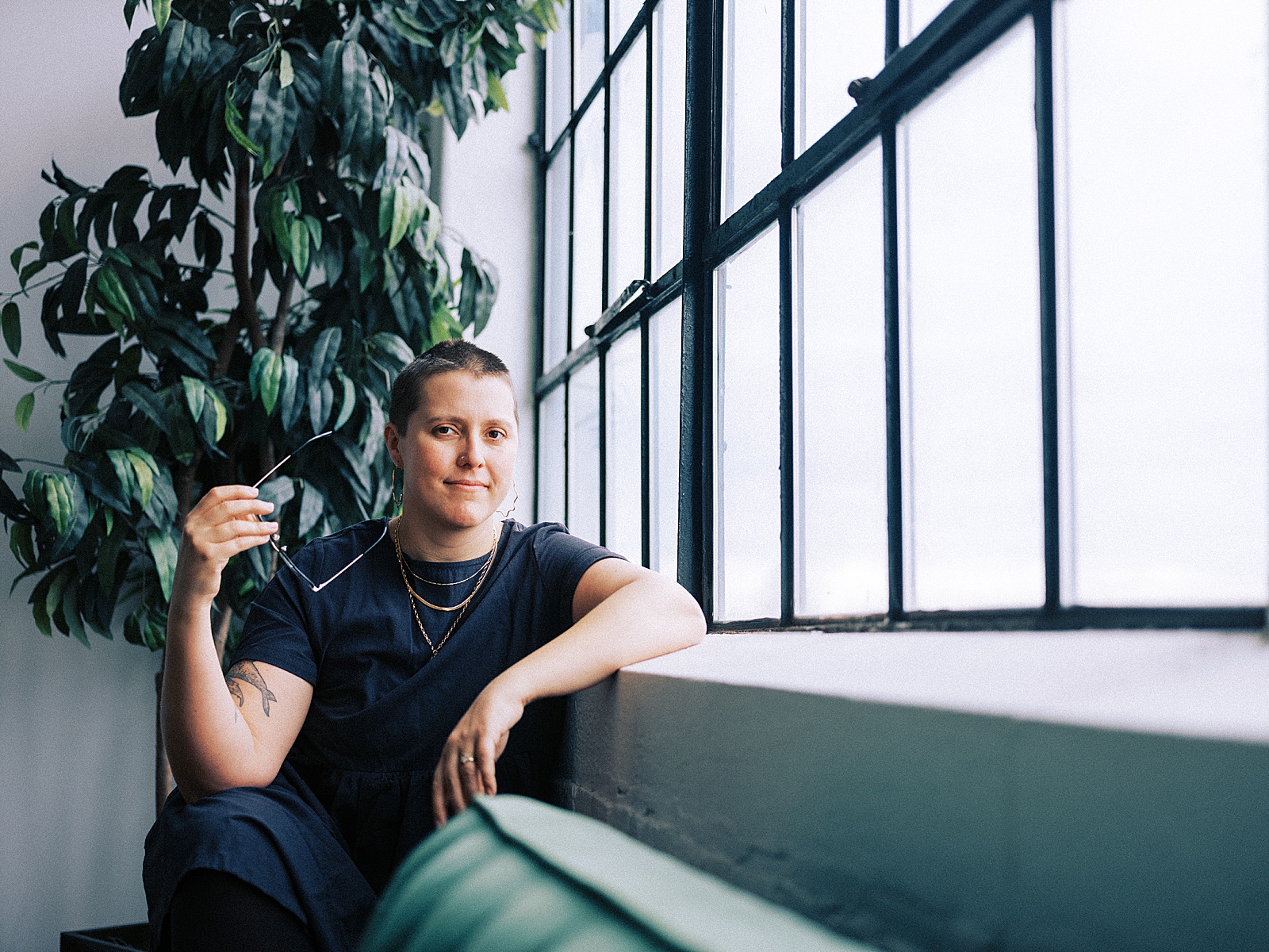 An ethical copywriter sits beside a window holding a pair of glasses.